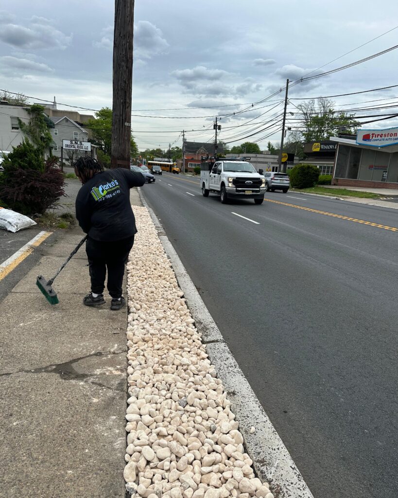 An employee of Clarke's professional team using a broom to clean the side of the road
