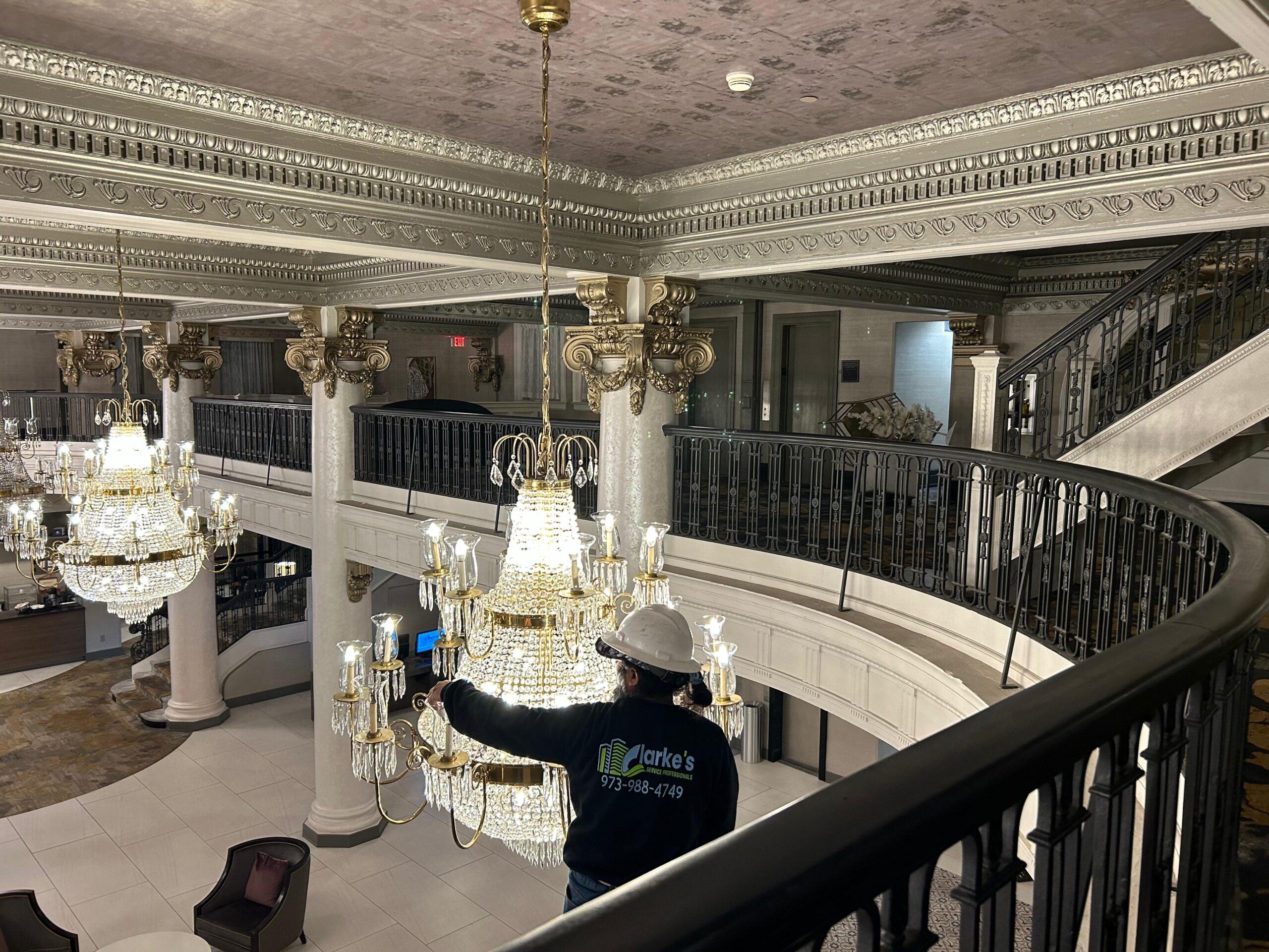 The Clarkes professional is standing on a ladder cleaning a large chandelier