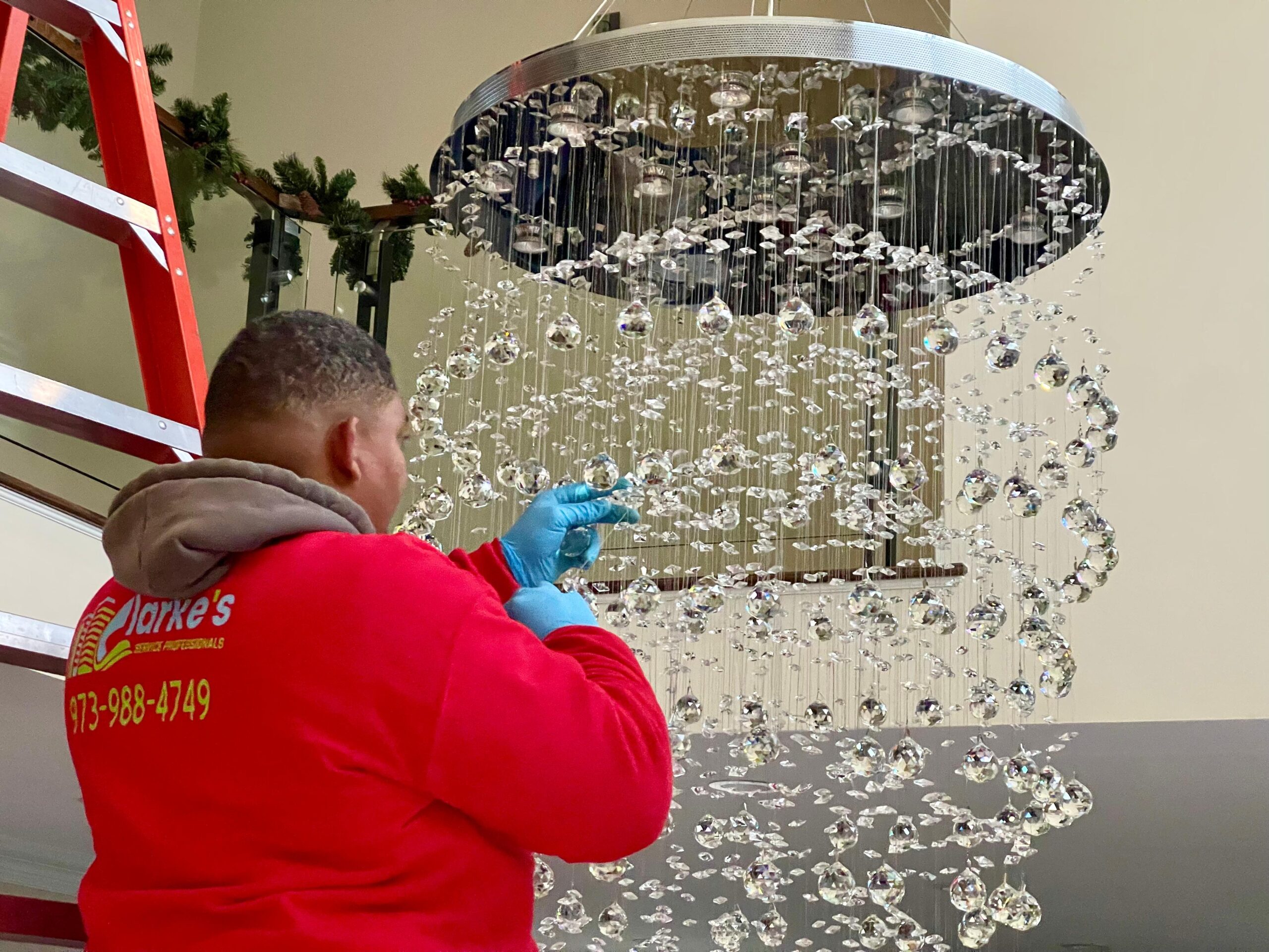 A Clarke's Service Professionals team member delicately cleaning a grand crystal chandelier.