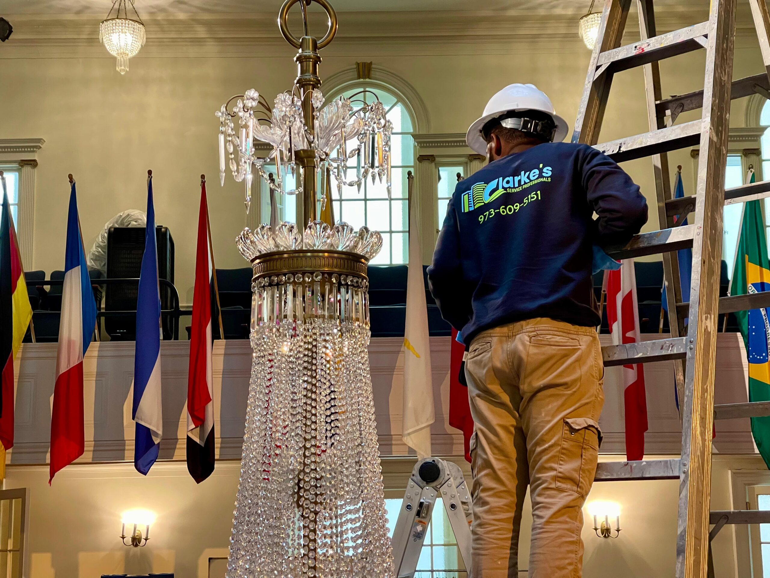 Clarke's Service Professional stands on a ladder next to a chandelier to clean it.