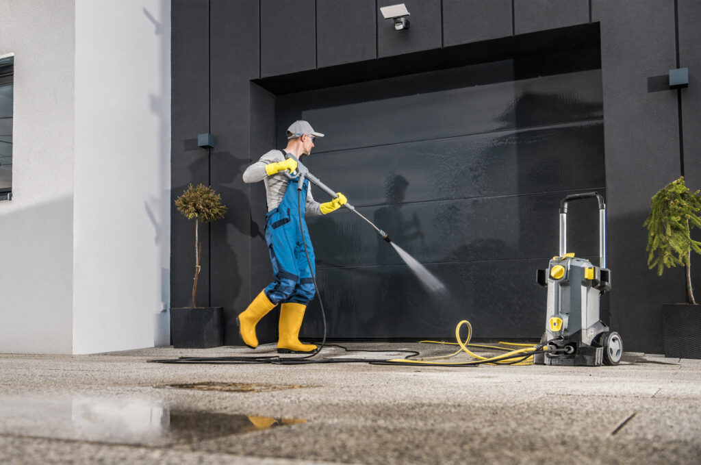 Caucasian Men Pressure Washing His Garage Gate Using Powerful Washer. Keeping the Gate and Driveway Clean.
