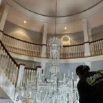 Crystal chandelier installation in a grand staircase. Worker in Clarke's Service Professionals.