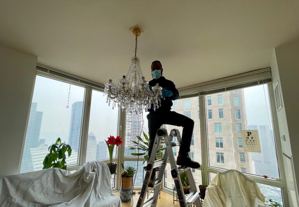 Clarke's Service Professionals Man on ladder cleaning crystal chandelier in modern apartment