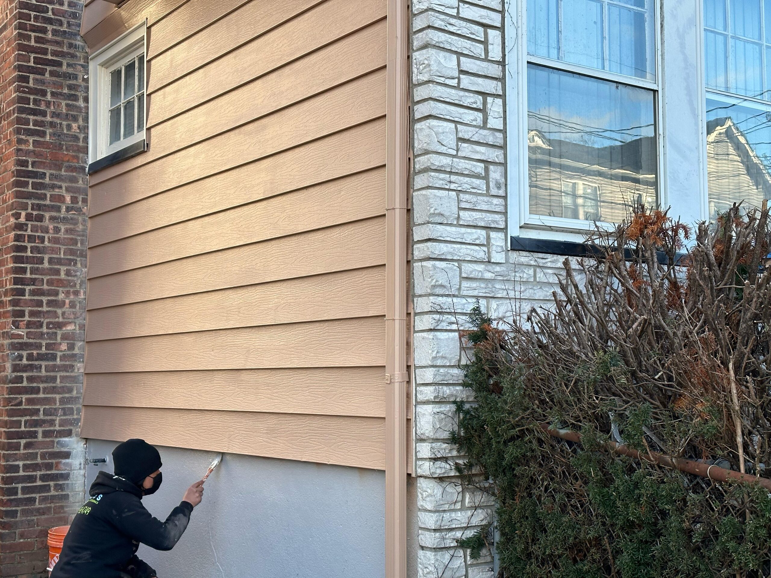 Clarke's Service Professionals Painter applying exterior paint to house siding