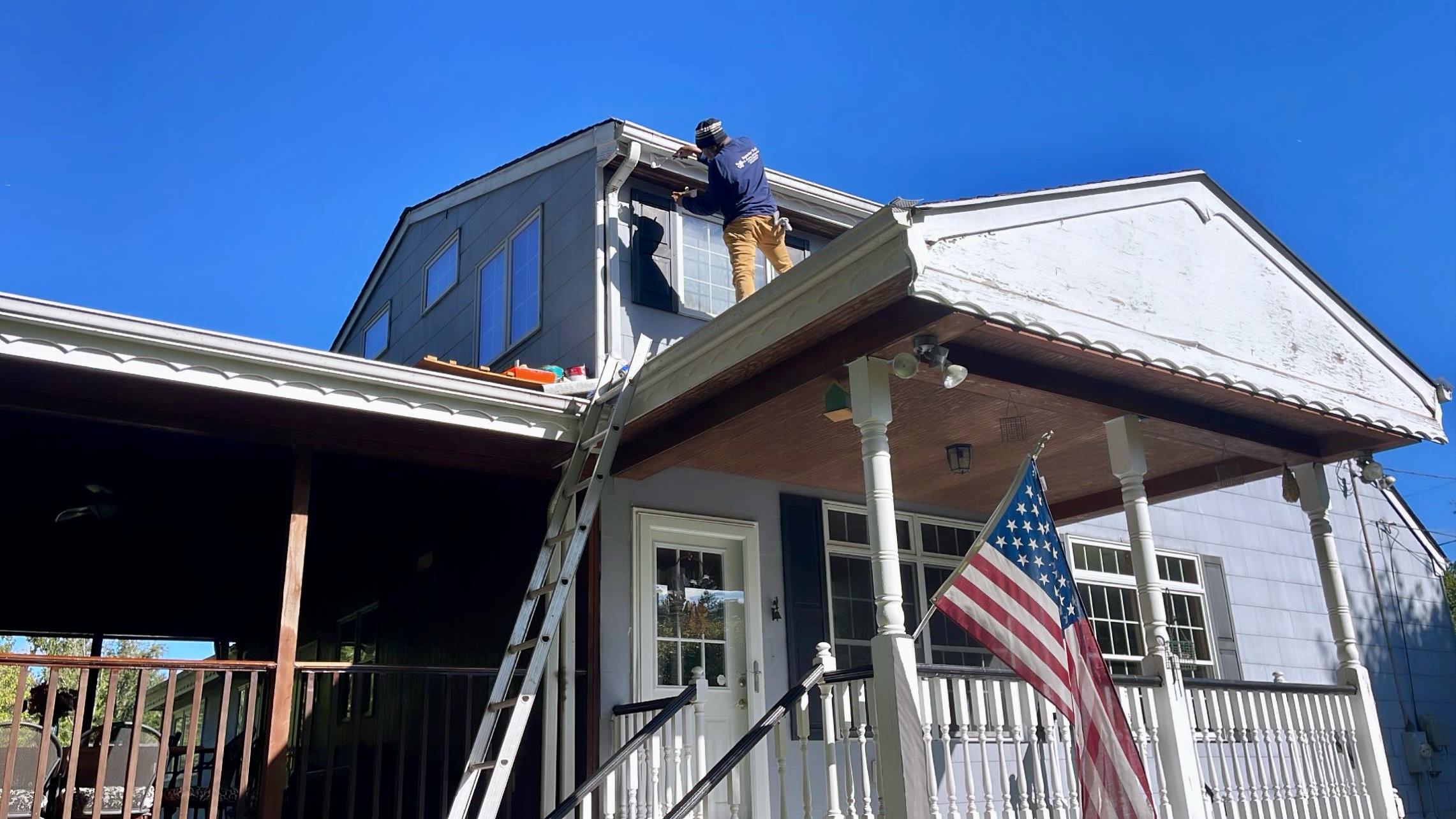 Clarke's Service Professionals Painter on ladder applying siding to house exterior
