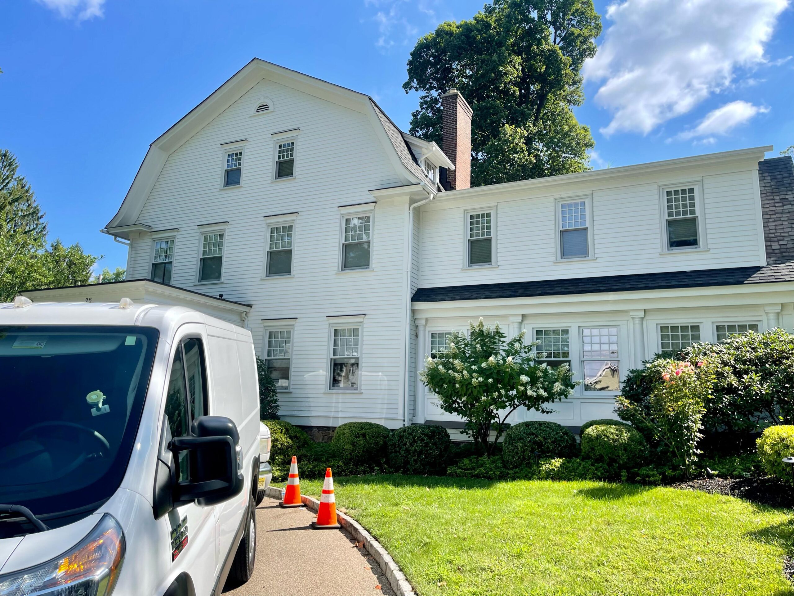 White colonial house exterior with landscaping, and a white van parked on the driveway.