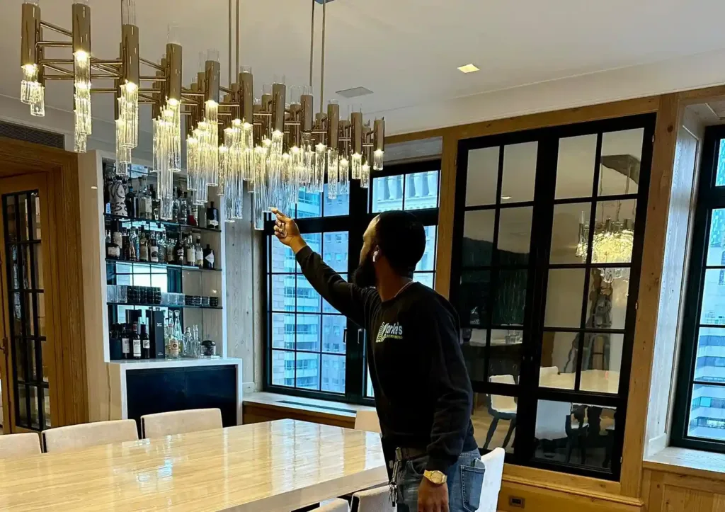 A clarkes handyman standing in front of a chandelier checking the cleanliness.