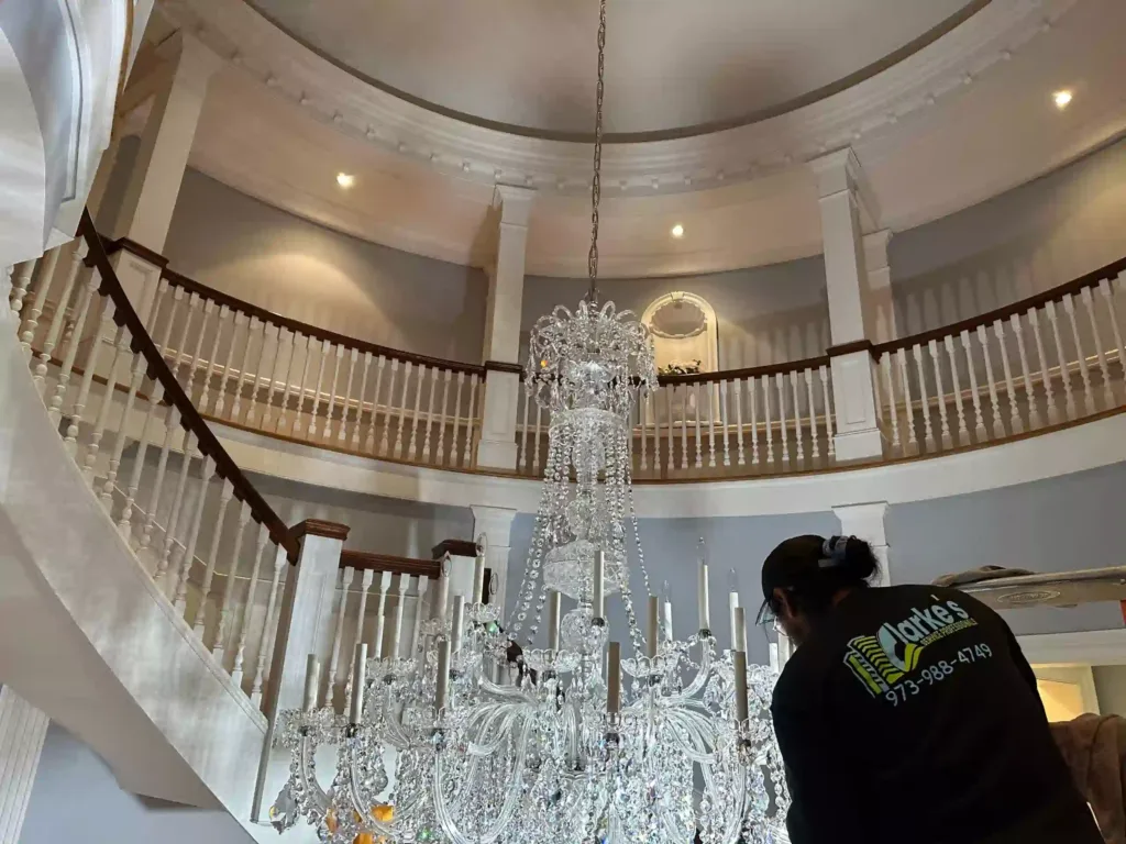 Worker cleaning a large crystal chandelier in a grand circular staircase