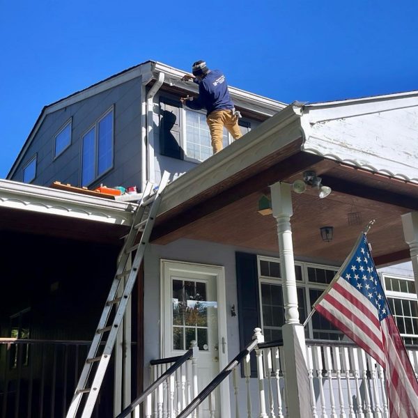 Clarke's Service Professionals Painter on ladder applying siding to house exterior