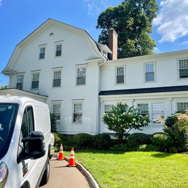 White colonial house exterior with landscaping, and a white van parked on the driveway.