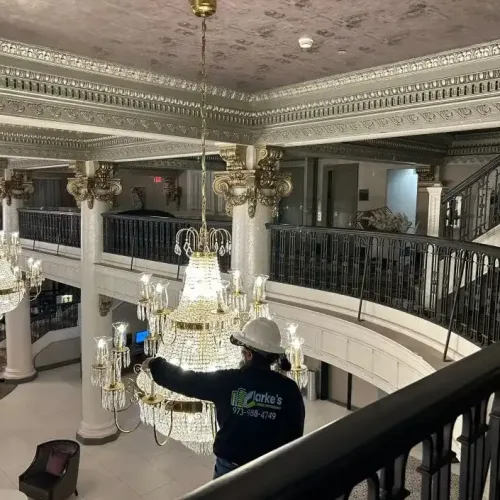 Clarke's Service Professionals Worker inspecting ornate chandelier in grand staircase interior