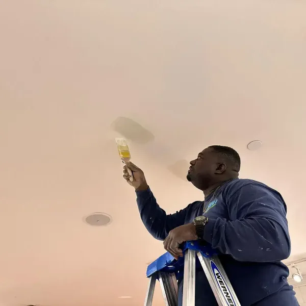 Man on ladder painting ceiling with brush, home renovation project.