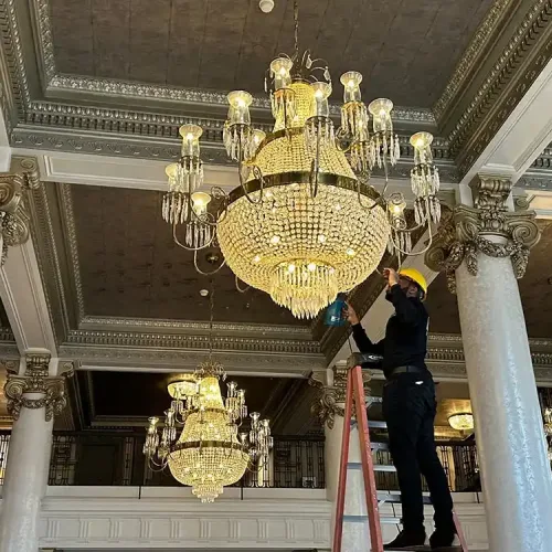 Clarke's Service Professionals Worker on ladder maintaining grand chandelier in ornate hall