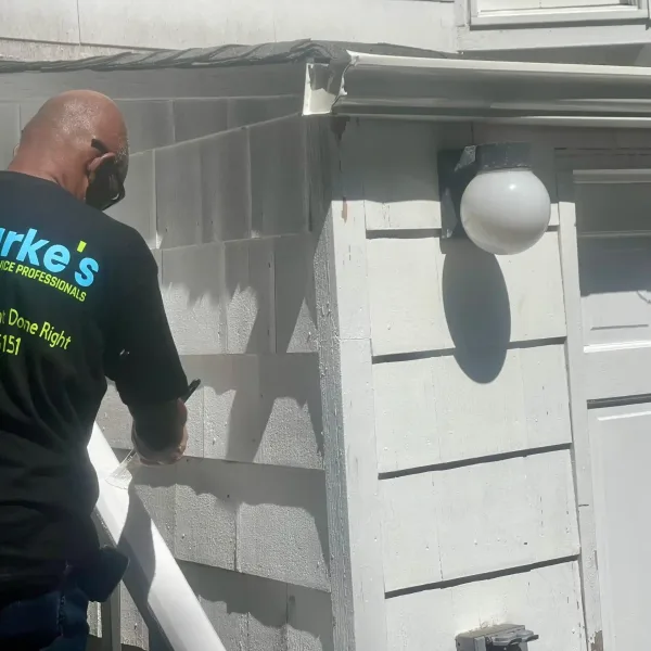 Clarke's Service Professionals Painter applying paint to house siding,
