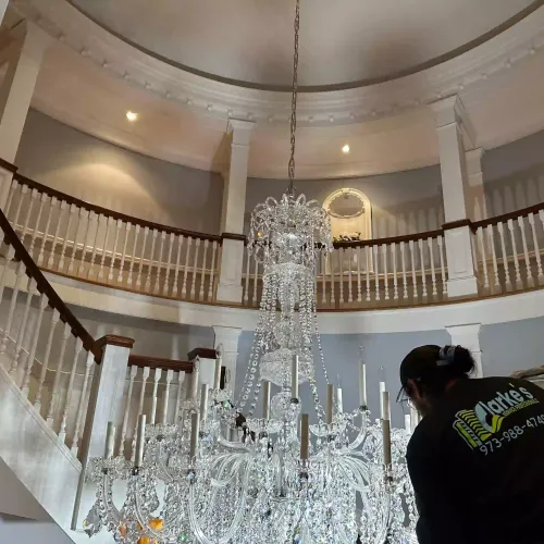 Worker cleaning a large crystal chandelier in a grand circular staircase
