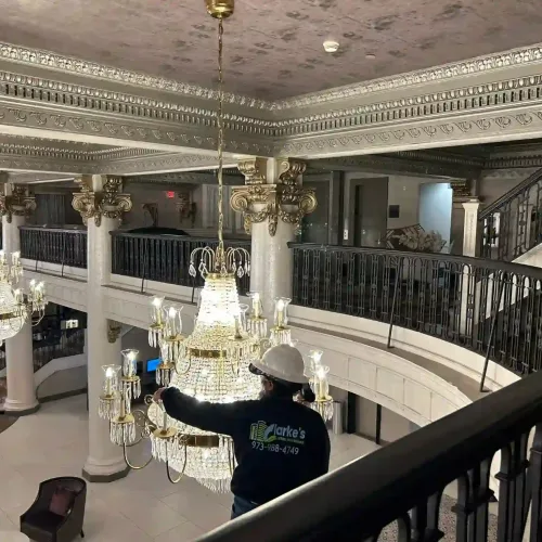 Clarke's Service Professionals Technician installing crystal chandeliers in a grand hotel lobby.