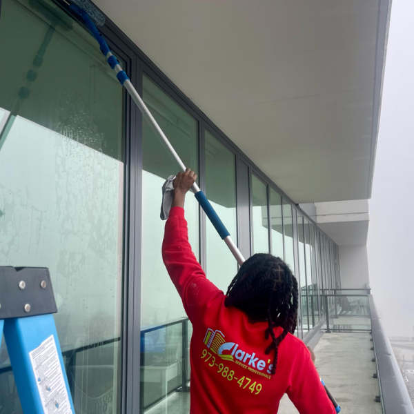 Window cleaner using a long-handled squeegee to clean a high-rise building's windows. Clarke's Service Professionals worker.